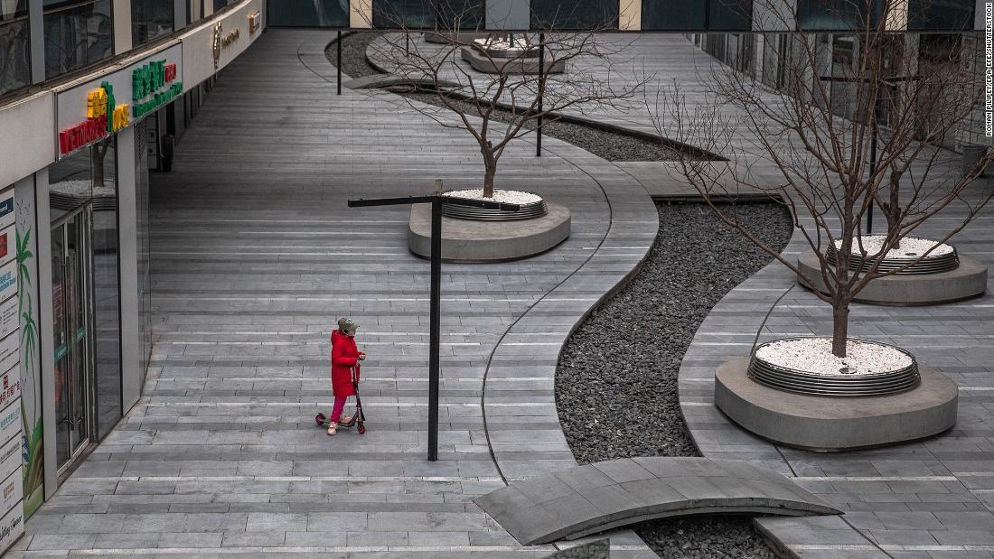 A child wearing a protective face mask rides on a scooter in an empty area in Beijing.